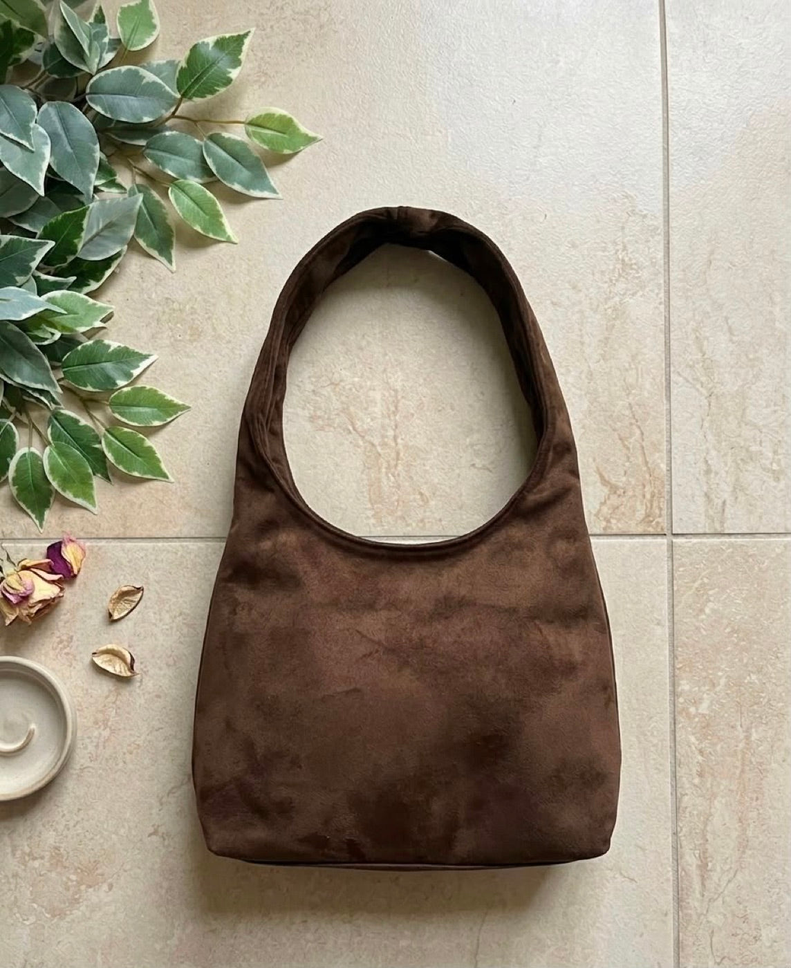 Brown suede hobo bag photographed with eucalyptus leaves and dried rose petals